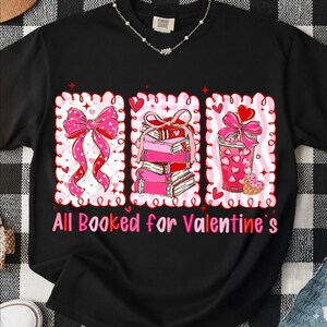 May include: Black t-shirt with a Valentine's Day graphic. The graphic features a pink bow, a stack of pink books, and a pink drink with hearts. The text "All Booked for Valentine's" is below the graphic.