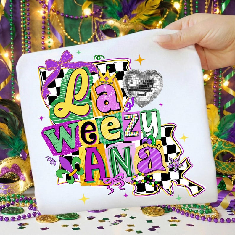 May include: White t-shirt with the text "La Weezu Ana" in colorful, block letters. The design includes a disco ball heart, a purple bow, and a checkered pattern, evoking a festive theme.