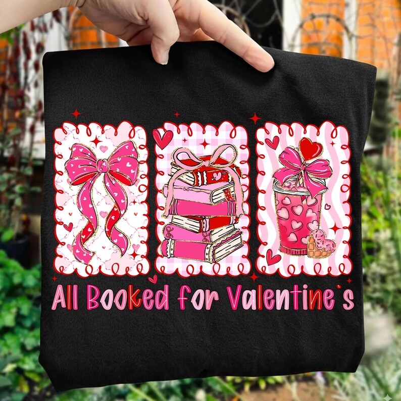 May include: Black t-shirt with a Valentine's Day graphic. The graphic features three framed images: a pink bow, a stack of books, and a heart-decorated drink. The text "All Booked for Valentine's" is printed in pink and red.
