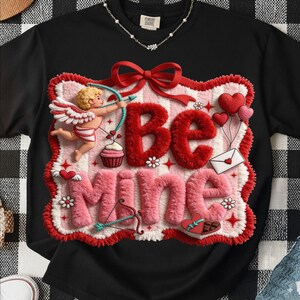 Peut inclure: T-shirt noir avec un motif de Saint-Valentin. Le motif pr&eacute;sente les mots "Be Mine" en rouge et rose, ainsi qu'un cupidon, des c&oelig;urs et un n&oelig;ud. Le t-shirt a un col rond et des manches courtes.