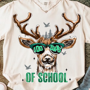 以下が含まれることがあります： クリーム色のTシャツ。サングラスをかけた鹿のグラフィックで、レンズには「100 Days」と書かれています。シャツには緑色の「OF SCHOOL」の文字と、鳥と木のイラストも描かれています。