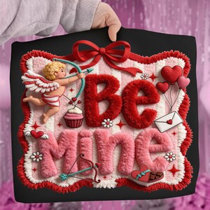 Peut inclure: Design carr&eacute; noir de la Saint-Valentin avec les mots "Be Mine" en rouge et rose, repr&eacute;sentant un cupidon, des c&oelig;urs, un cupcake et un n&oelig;ud. Le design a un aspect textur&eacute; et moelleux avec une bordure rouge et blanche.