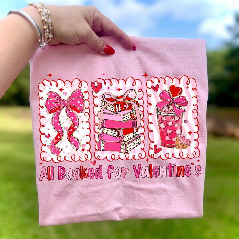May include: Pink t-shirt with a Valentine's Day theme. The shirt features three framed illustrations: a bow, a stack of books, and a drink, all with hearts. The text "All Booked for Valentine's" is printed at the bottom.