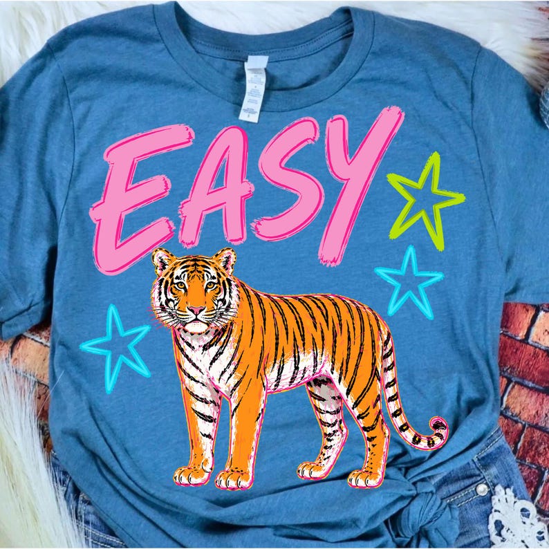 May include: Blue t-shirt with a tiger graphic. The word "EASY" is written in pink, outlined in white, above the tiger. Two blue and one yellow star are also on the shirt.