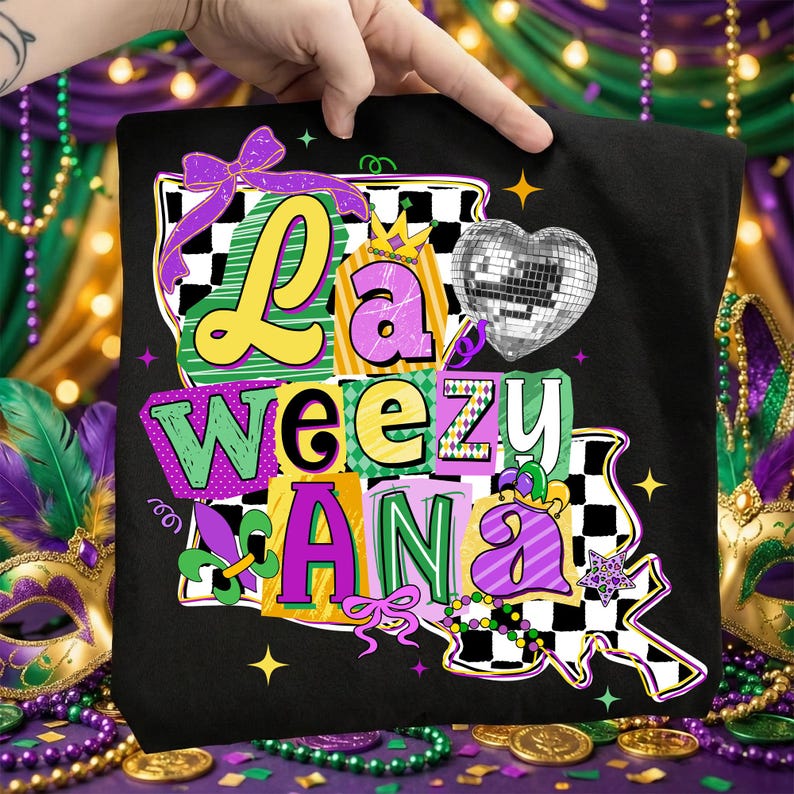 May include: Black t-shirt with a colorful graphic design. The design features the words "La Weez Ana" in various colors and fonts, along with a disco ball heart, bows, and a fleur-de-lis. The design is in the style of a Mardi Gras celebration.