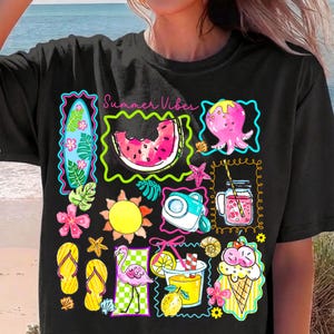 Puede incluir: Camiseta negra con un gr&aacute;fico colorido de tem&aacute;tica veraniega. El dise&ntilde;o incluye una rodaja de sand&iacute;a, un pulpo, un cono de helado, un flamenco y el texto "Summer Vibes". Otros elementos incluyen una tabla de surf, un sol y chanclas.