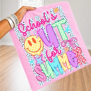 Puede incluir: Manta rosa con las palabras "School's Out for Summer" en letras coloridas y juguetonas. El dise&ntilde;o incluye una carita sonriente, estrellas, flores y lazos. La manta tiene un fondo a rayas y lunares.