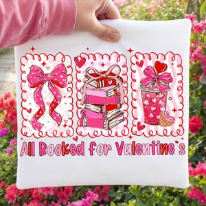 May include: White pillow with a Valentine's Day design. The design includes a pink bow, a stack of pink books, and a pink drink with a heart-shaped cookie. The text "All Booked for Valentine's" is printed in pink.