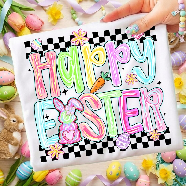Może przedstawiać: Biała koszulka z kolorową grafiką "Happy Easter". Projekt zawiera pastelowe litery, marchewkę, pisanki i kr&oacute;lika. Koszulka ma czarno-białą szachownicę i jest otoczona dekoracjami wielkanocnymi.