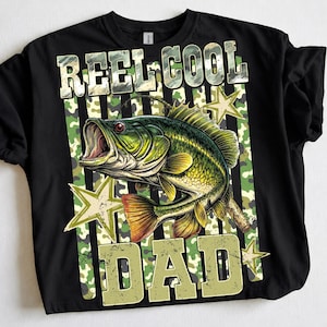 May include: Black t-shirt with a graphic of a green and yellow fish with an open mouth, surrounded by stars and camouflage stripes. The text "REEL COOL DAD" is printed above and below the fish in a distressed font.