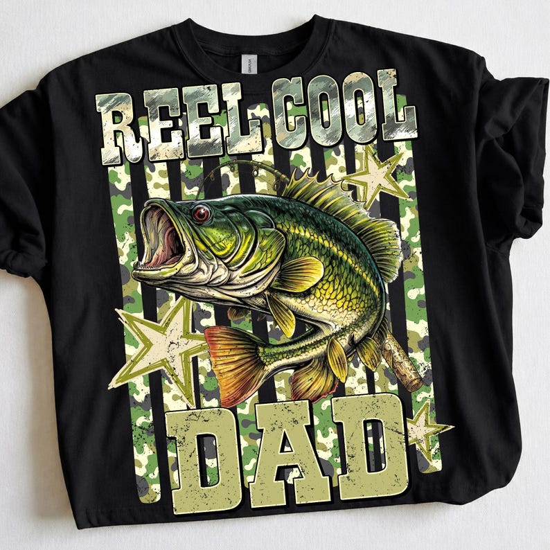 May include: Black t-shirt with a graphic of a green and yellow fish with an open mouth, surrounded by stars and camouflage stripes. The text "REEL COOL DAD" is printed above and below the fish in a distressed font.