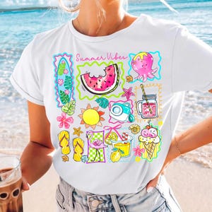 Puede incluir: Camiseta blanca con un colorido dise&ntilde;o de tem&aacute;tica veraniega. El dise&ntilde;o incluye una rodaja de sand&iacute;a, un pulpo, un sol, una c&aacute;mara y otros iconos veraniegos. Las palabras "Summer Vibes" est&aacute;n impresas encima del dise&ntilde;o.
