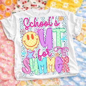 Puede incluir: Camiseta blanca con un gr&aacute;fico colorido que dice "School's Out for Summer". El dise&ntilde;o incluye una carita sonriente, flores, estrellas y las palabras en varios colores y patrones. La camiseta est&aacute; doblada.