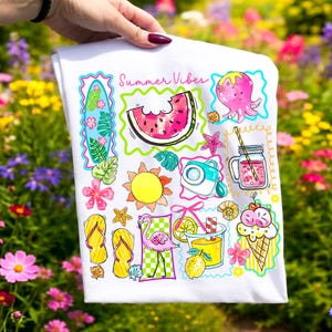 Puede incluir: Toalla blanca con ilustraciones coloridas de verano. Presenta una rodaja de sand&iacute;a, sol, flamenco, helado y el texto "Summer Vibes". El dise&ntilde;o incluye una tabla de surf, c&aacute;mara y una bebida con pajita.