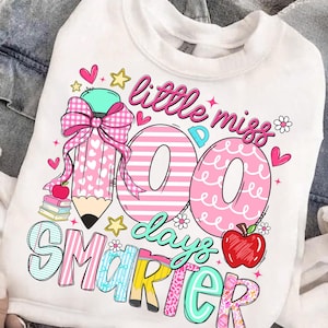 Puede incluir: Sudadera blanca con un dise&ntilde;o gr&aacute;fico colorido. El dise&ntilde;o incluye el texto "little miss 100 days smarter" con un l&aacute;piz grande, corazones, estrellas y una manzana. Los n&uacute;meros "100" son de color rosa.