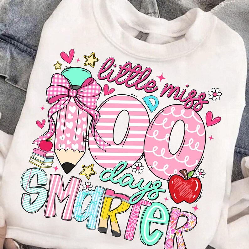 Puede incluir: Sudadera blanca con un dise&ntilde;o gr&aacute;fico colorido. El dise&ntilde;o incluye el texto "little miss 100 days smarter" con un l&aacute;piz grande, corazones, estrellas y una manzana. Los n&uacute;meros "100" son de color rosa.