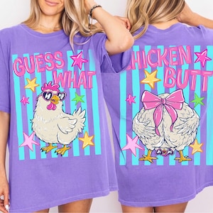 May include: A purple t-shirt with a graphic design featuring a cartoon chicken wearing sunglasses and the text "GUESS WHAT" on the front. The back of the shirt has a chicken butt graphic and the text "CHICKEN BUTT".