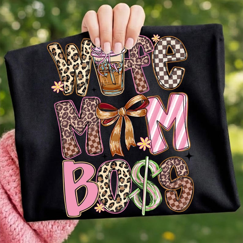 May include: Black t-shirt with the words "Wife Mom Boss" in a mix of fonts and patterns. The design includes a coffee drink, a bow, and a dollar sign. The letters have leopard print, checkered, and striped designs.