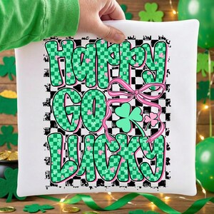 May include: White square pillow with the text "Happy Go Lucky" in green and pink, with a checkered background. The design includes a pink bow and shamrocks, perfect for St. Patrick's Day.