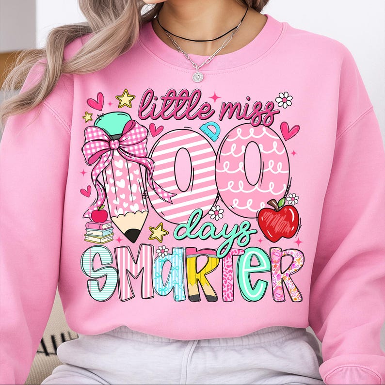 Puede incluir: Sudadera rosa con el texto "little miss 100 days smarter". El dise&ntilde;o incluye un l&aacute;piz, el n&uacute;mero 100, una manzana, estrellas y corazones. La sudadera es de cuello redondo.