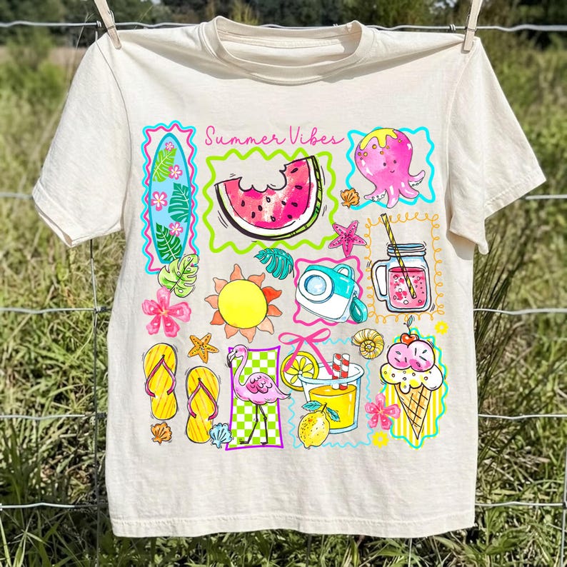 Puede incluir: Camiseta color crema con un gr&aacute;fico colorido de tem&aacute;tica veraniega. El dise&ntilde;o incluye una rodaja de sand&iacute;a, un pulpo, un cono de helado y el texto "Summer Vibes". La camiseta est&aacute; colgada en un tendedero.