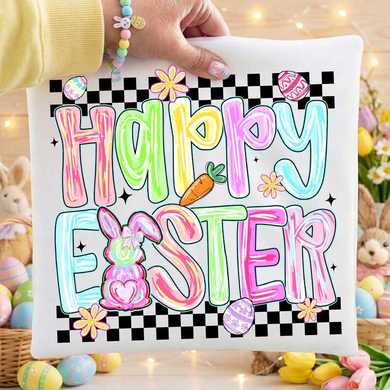 Może przedstawiać: Biała kwadratowa poduszka z napisem "Happy Easter" w kolorowych literach bąbelkowych. Projekt zawiera kr&oacute;lika, marchewkę, kwiaty i pisanki, wszystko na czarno-białej szachownicy.