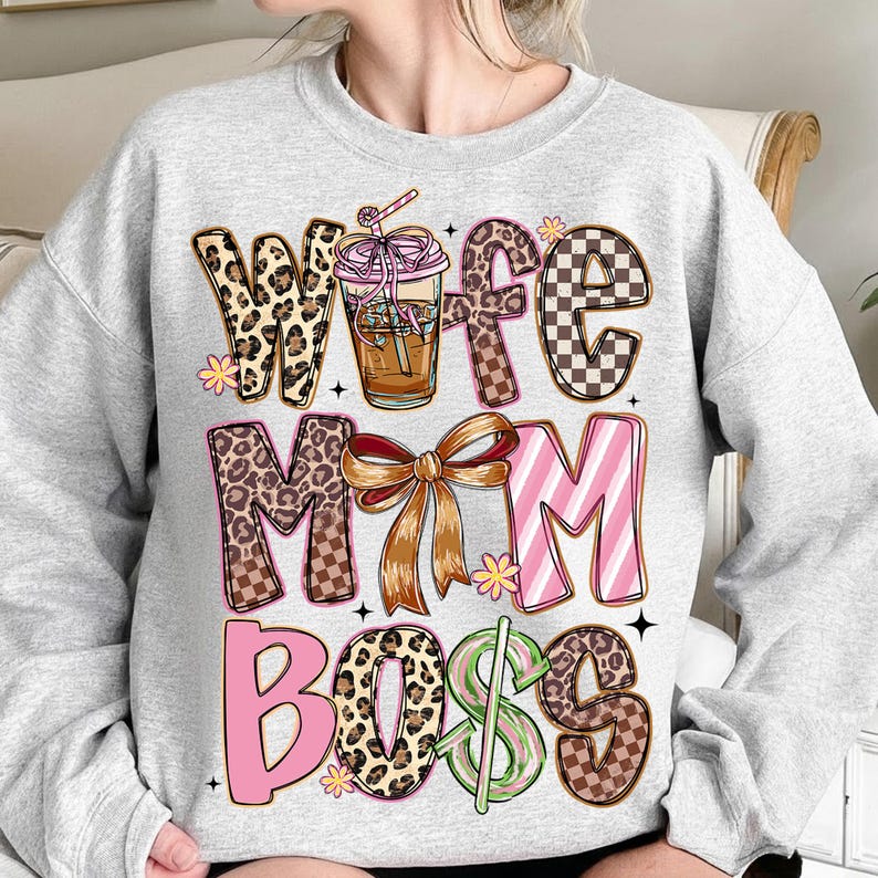 May include: A light gray sweatshirt with the words "Wife Mom Boss" in a mix of leopard print, checkered, and striped patterns. A coffee drink graphic is in the center, with a bow and floral accents.