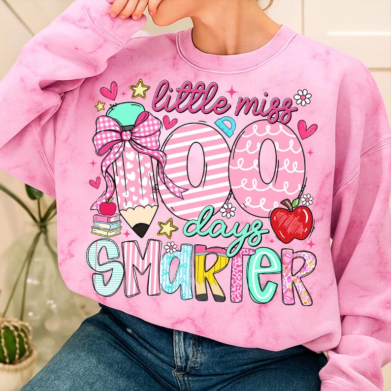 Puede incluir: Sudadera rosa te&ntilde;ida con un gr&aacute;fico colorido. El gr&aacute;fico incluye el texto "little miss 100 days smarter" con un l&aacute;piz, corazones, estrellas y una manzana. La sudadera es de cuello redondo.