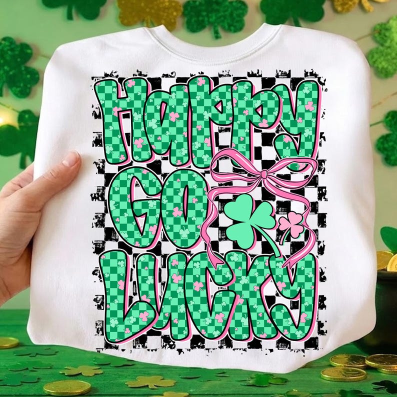 May include: White sweatshirt with the text "Happy Go Lucky" in green checkered letters with pink shamrocks. A pink bow and shamrock graphic are also featured. The design is set against a black and white checkered background.