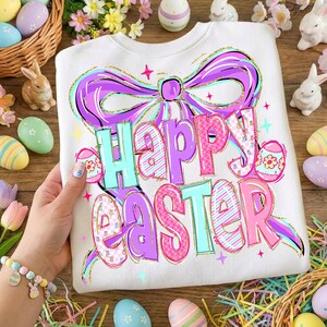 May include: White sweatshirt with a colourful "Happy Easter" graphic. The design features a large purple bow, Easter eggs, and the text in shades of pink, blue, and purple. Easter-themed apparel.