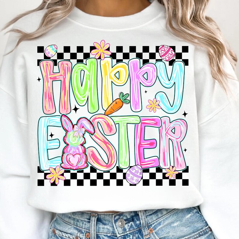 Może przedstawiać: Biała bluza z kolorową grafiką "Happy Easter". Projekt zawiera pastelowe litery, kr&oacute;lika, marchewkę i pisanki, wszystko na czarno-białym szachownicowym obramowaniu. Swobodny, świąteczny element garderoby.