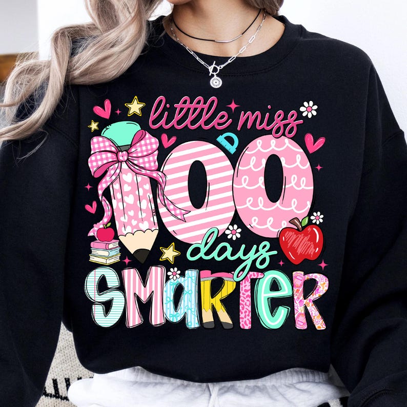 Puede incluir: Sudadera negra con un dise&ntilde;o gr&aacute;fico colorido. El dise&ntilde;o incluye el texto "little miss 100 days smarter" con un l&aacute;piz, corazones y una manzana. Los n&uacute;meros "100" son de rayas rosas y blancas.
