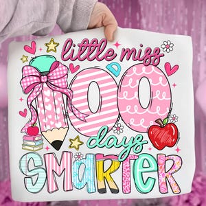 Puede incluir: Bolso tote blanco con un dise&ntilde;o colorido que celebra los 100 d&iacute;as de escuela. Presenta un gran l&aacute;piz rosa, las palabras "little miss 100 days smarter", corazones, estrellas y una manzana.