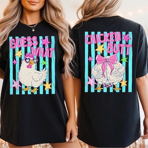 May include: Black t-shirt with a whimsical design featuring a cartoon chicken wearing sunglasses and the text "GUESS WHAT" on the front. The back of the shirt displays a chicken's rear with a pink bow and the words "CHICKEN BUTT".
