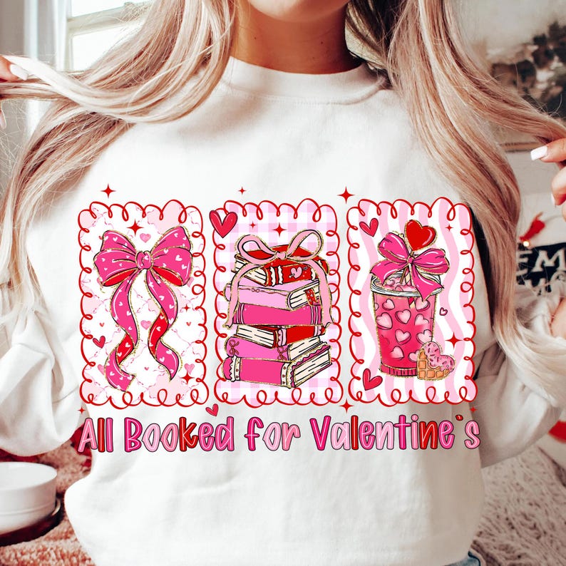 May include: White sweatshirt with a Valentine's Day graphic. The graphic features a pink bow, a stack of pink books, and a pink coffee cup, all within decorative frames. The text "All Booked for Valentine's" is at the bottom.