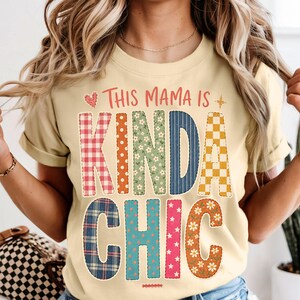 May include: A light yellow t-shirt featuring the text "THIS MAMA IS KINDA CHIC" in large, multi-patterned block letters. The letters display various designs including red gingham, orange polka dots, green floral, blue stripes, and yellow checkerboard.