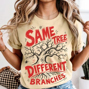 May include: A pale yellow t-shirt featuring the text "SAME TREE DIFFERENT BRANCHES" in red, with a black tree illustration. The top has short sleeves and a round neckline.