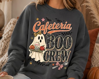 May include: A dark gray crewneck sweatshirt featuring a graphic print of a ghost wearing a leopard print bow, holding a cafeteria tray with a milk carton, pumpkin, and apple. The text reads Cafeteria BOO CREW, accented by bats, stars, and a spoon.