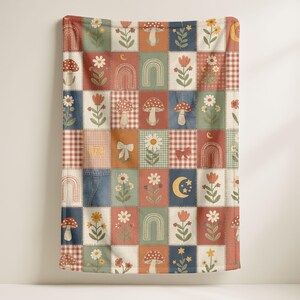 May include: A patchwork blanket featuring squares with floral, mushroom, and rainbow designs. The blanket has a mix of colors including red, green, blue, and orange. The squares are stitched together with a visible seam.
