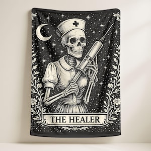 Puede incluir: Manta en blanco y negro con un esqueleto con uniforme de enfermera sosteniendo una jeringa. El diseño incluye una luna creciente, estrellas y un borde floral. El texto "THE HEALER" se muestra en la parte inferior.
