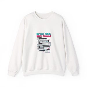 以下が含まれることがあります： 積み重ねられたコンピューターのエラーメッセージウィンドウのグラフィックが特徴の白いスウェットシャツ。「Error 404: Not Found」の文字が、ターコイズとピンクでウィンドウの上にあります。スウェットシャツはクルーネックと長袖です。