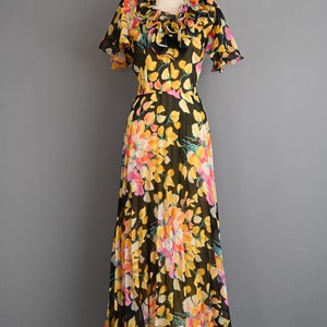 May include: A black maxi dress with a floral print in shades of yellow, pink, and orange. The dress has a ruffled neckline and short sleeves.
