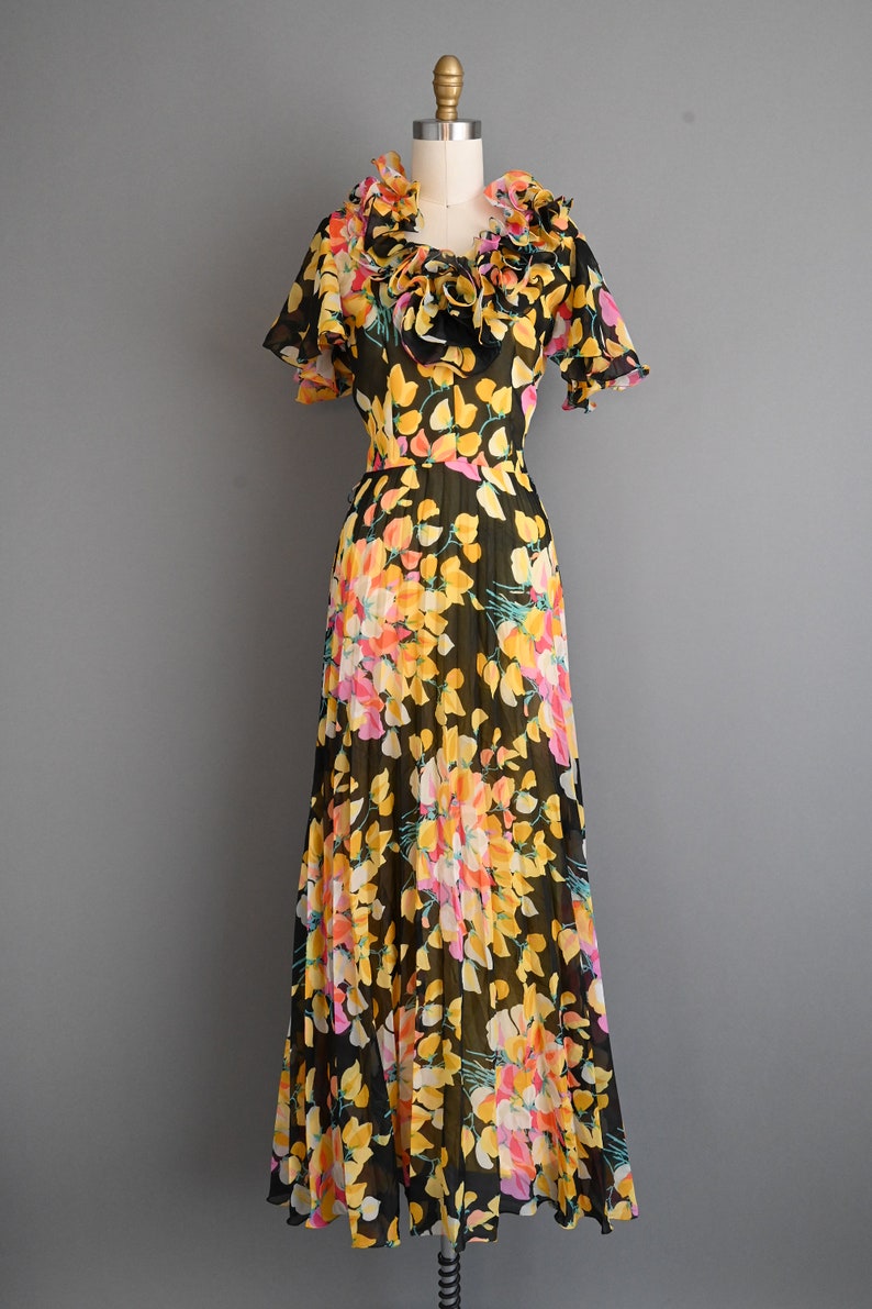 May include: A black maxi dress with a floral print in shades of yellow, pink, and orange. The dress has a ruffled neckline and short sleeves.