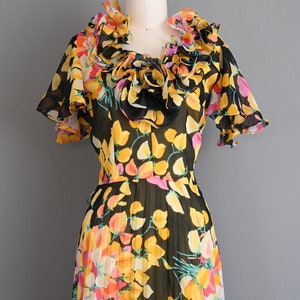 May include: A black and yellow floral print dress with a ruffled neckline and short sleeves. The dress is made of a sheer fabric and has a pleated skirt.