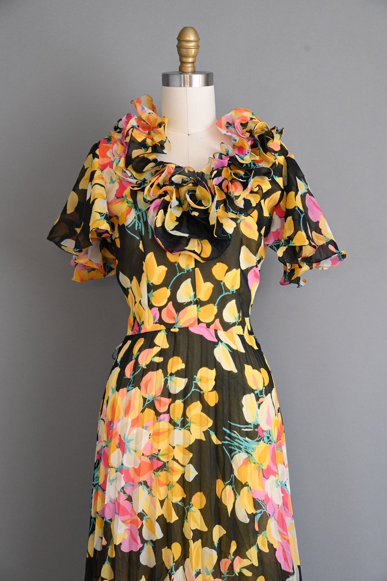 May include: A black and yellow floral print dress with a ruffled neckline and short sleeves. The dress is made of a sheer fabric and has a pleated skirt.