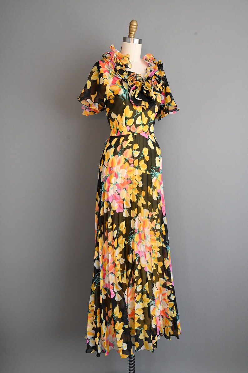 May include: A black maxi dress with a floral print featuring yellow, pink, and orange flowers. The dress has a ruffled neckline and short sleeves.