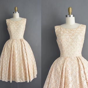 May include: A sleeveless, ivory lace dress with a fitted bodice and a full, gathered skirt. The dress has a simple, elegant design.