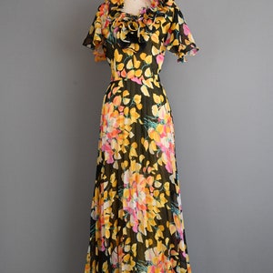 May include: A black maxi dress with a floral print featuring yellow, pink, and orange flowers. The dress has a ruffled neckline and short sleeves.