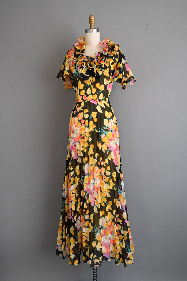 May include: A black maxi dress with a floral print featuring yellow, pink, and orange flowers. The dress has a ruffled neckline and short sleeves.
