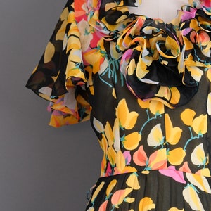 May include: A black sheer dress with a floral print in yellow, pink, and white. The dress has a ruffled neckline and short sleeves.